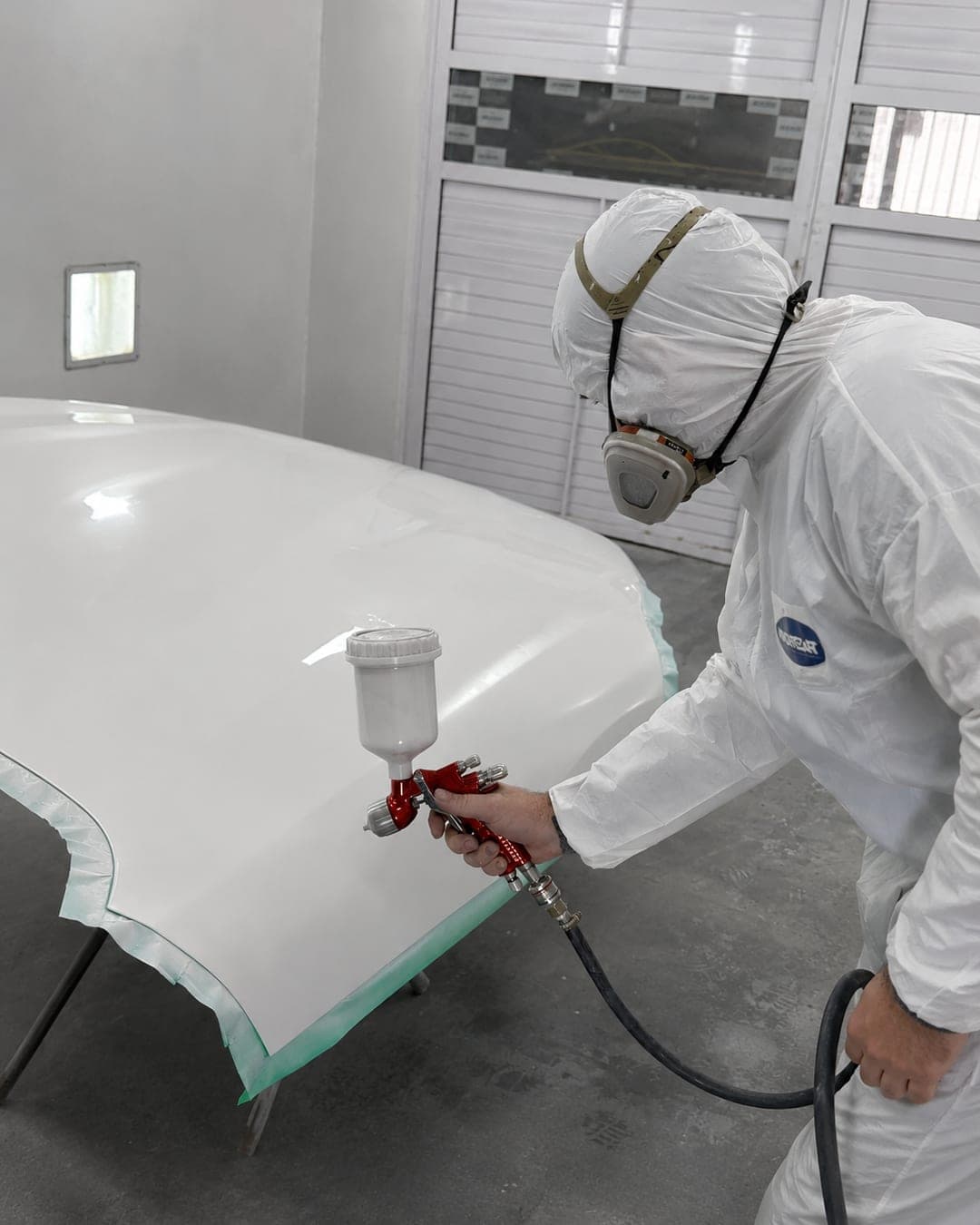 Pintor com equipamento de proteção aplicando pintura automotiva na Exclusive Auto Reparos